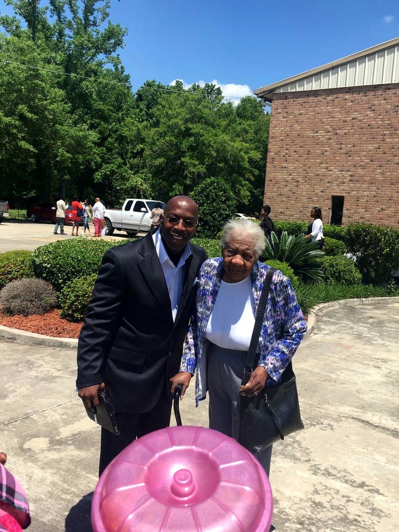 Doc Lewis in a suit standing beside an older woman outside a brick building