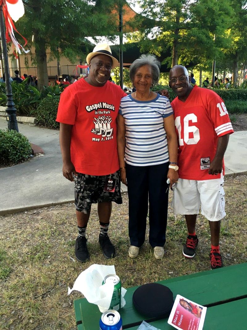 Doc Lewis in a red number 16 jersey with two friends at an outdoor gathering, one wearing a Gospel Music in the Park shirt