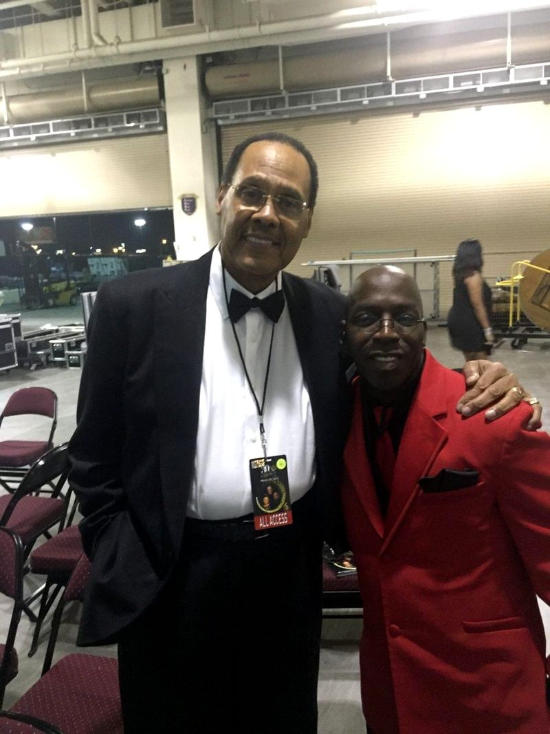 Doc Lewis in a red jacket with his arm around a friend in a tuxedo