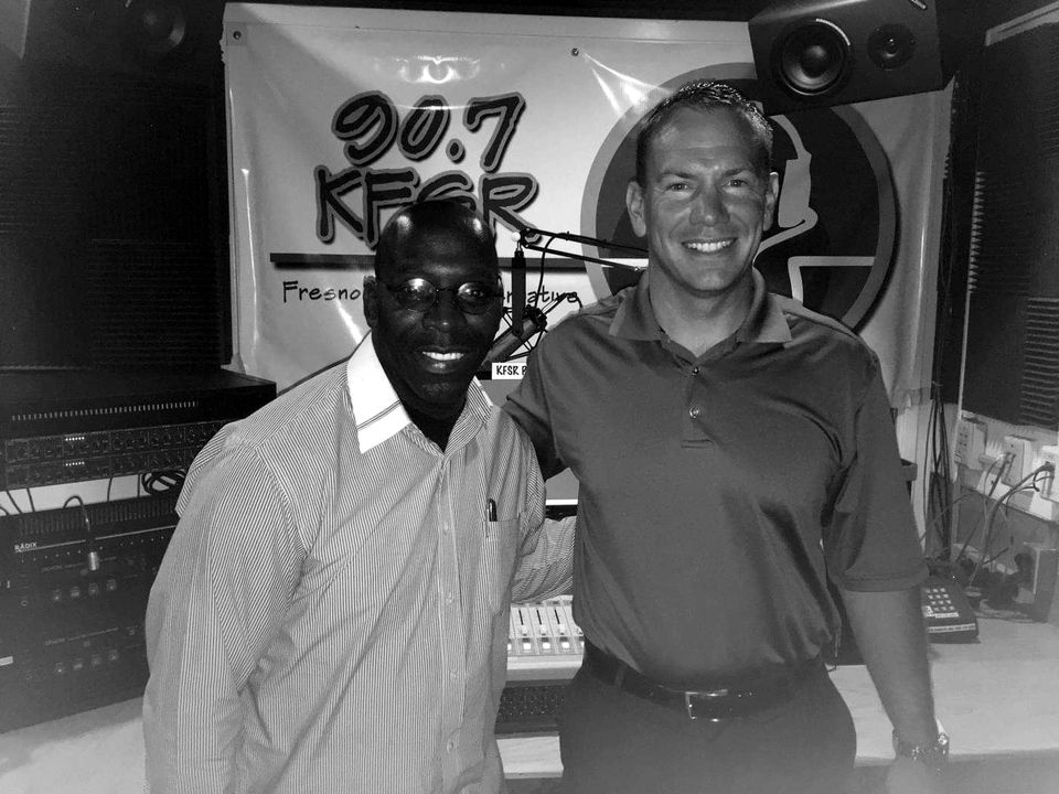 Doc Lewis with a guest in front of a 90.7 KFSR banner in the station studio
