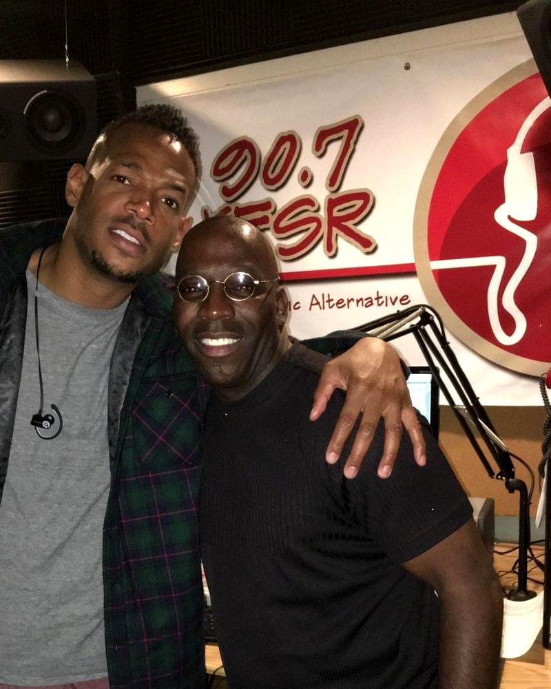 Doc Lewis with a guest in the 90.7 KFSR studio, the station logo on the wall behind them