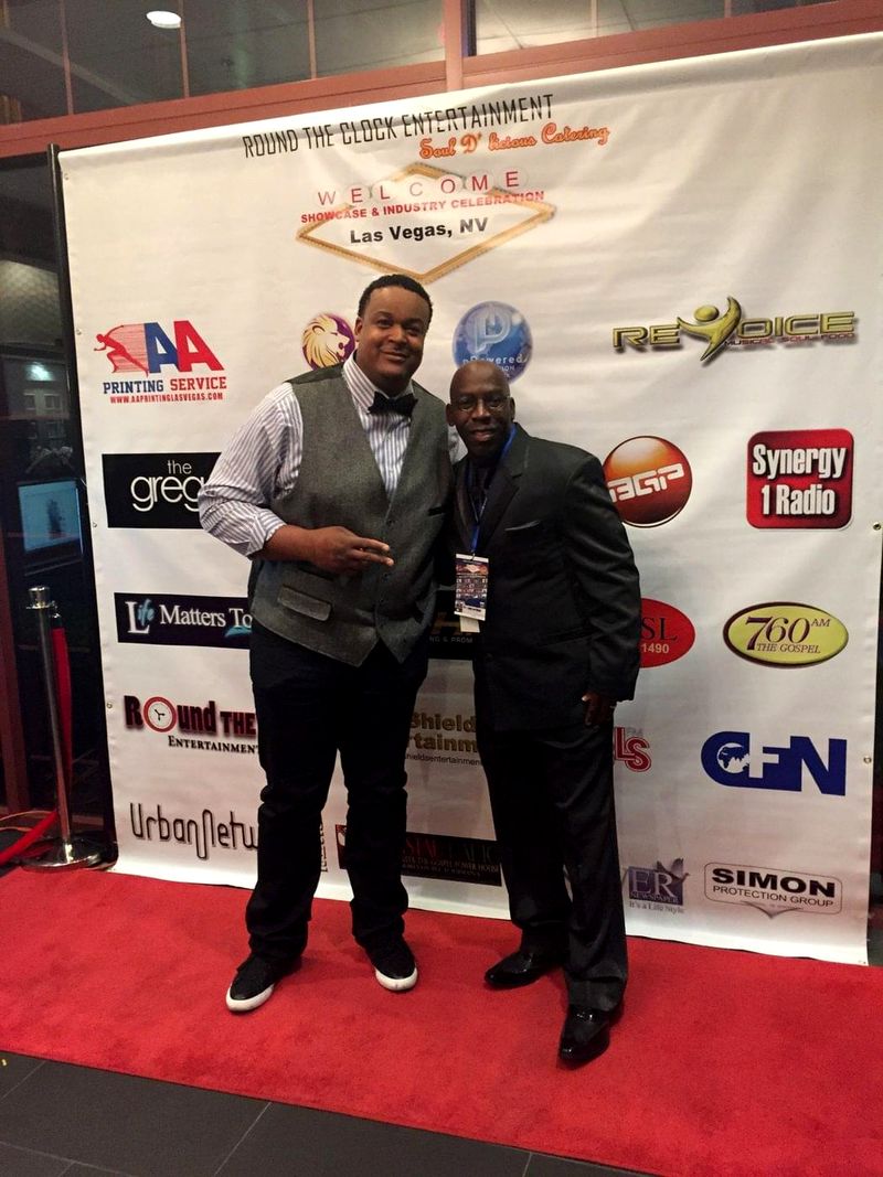 Doc Lewis with a friend on a red carpet in front of a backdrop of radio and media sponsors