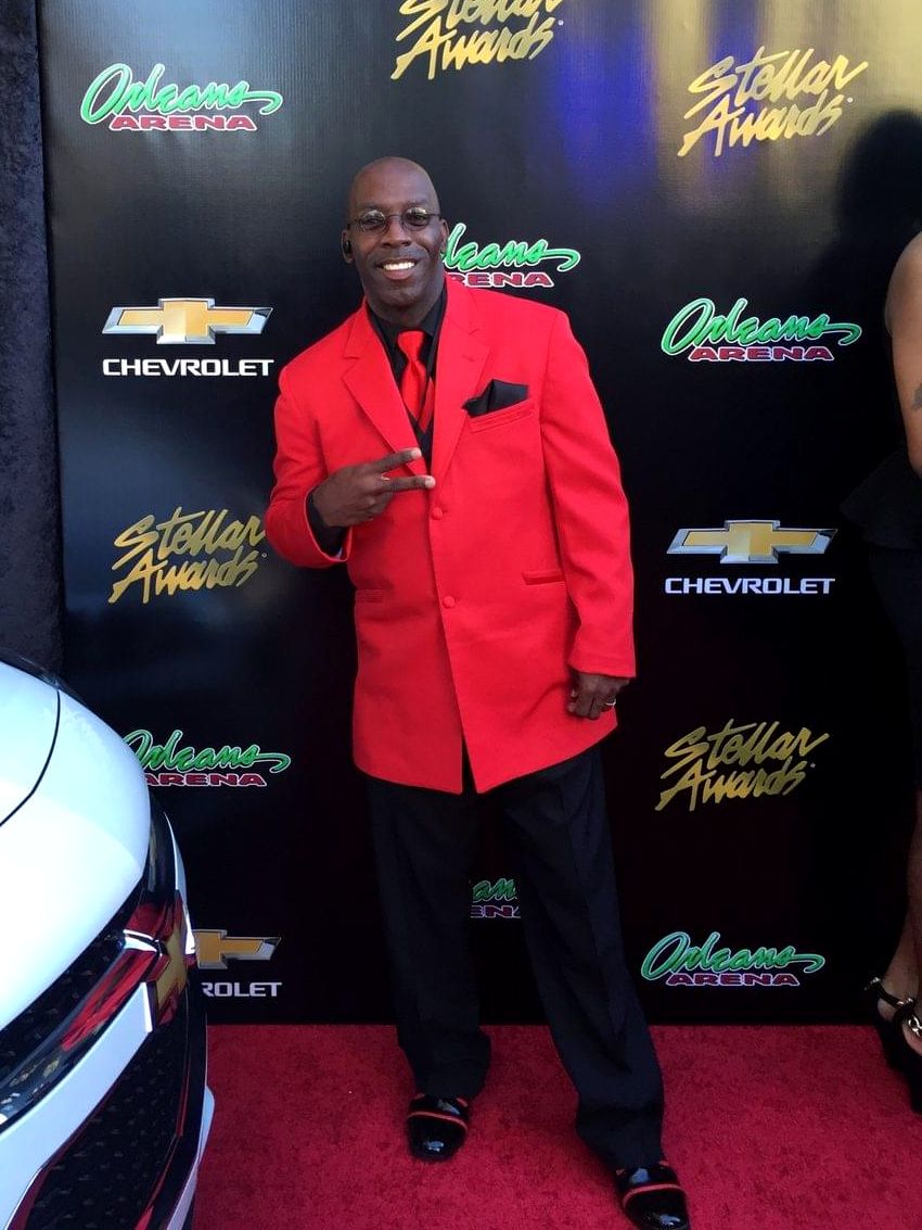 Doc Lewis in a red suit on a red carpet in front of a Stellar Awards backdrop