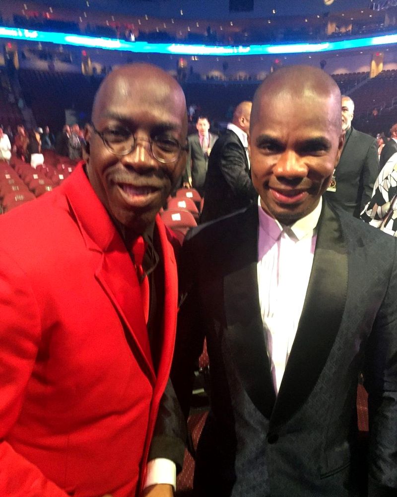 Doc Lewis in a red suit, smiling with a friend inside an arena