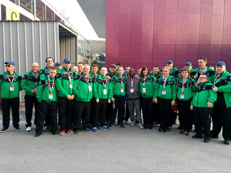A large delegation of athletes in green jackets posing together at the Games in Austria