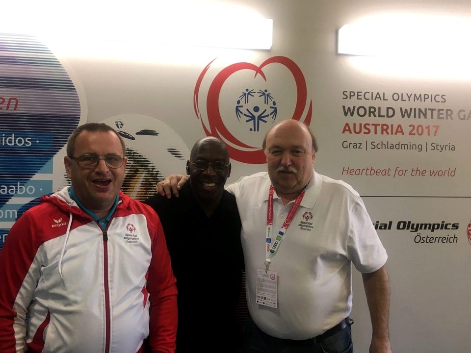 Doc Lewis with two men in Special Olympics Austria jackets in front of the World Winter Games 2017 banner