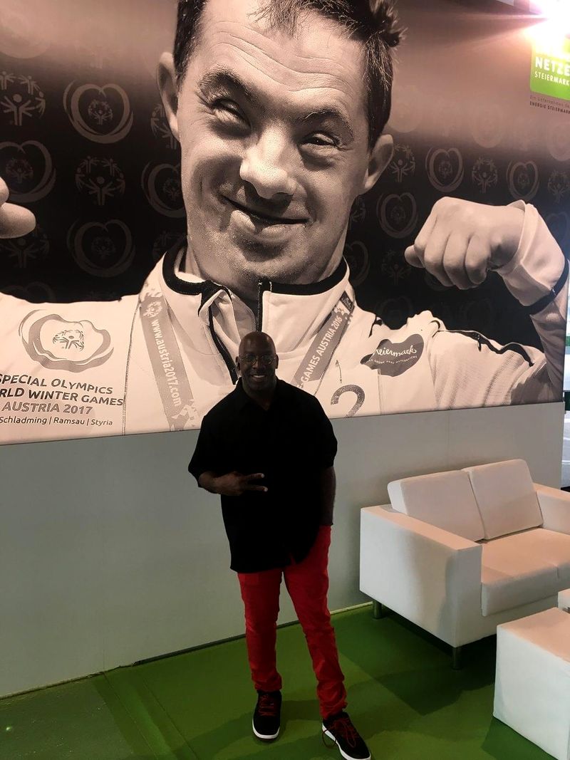 Doc Lewis standing in front of a giant poster of a smiling Special Olympics athlete in Austria