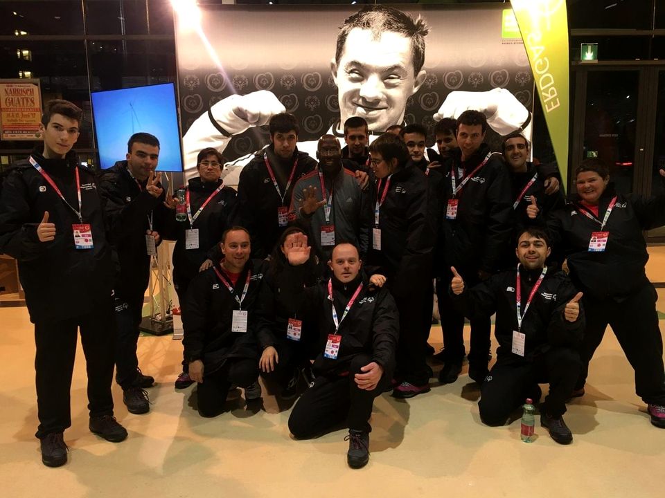Doc Lewis with a large team of athletes giving thumbs up in front of a giant athlete poster