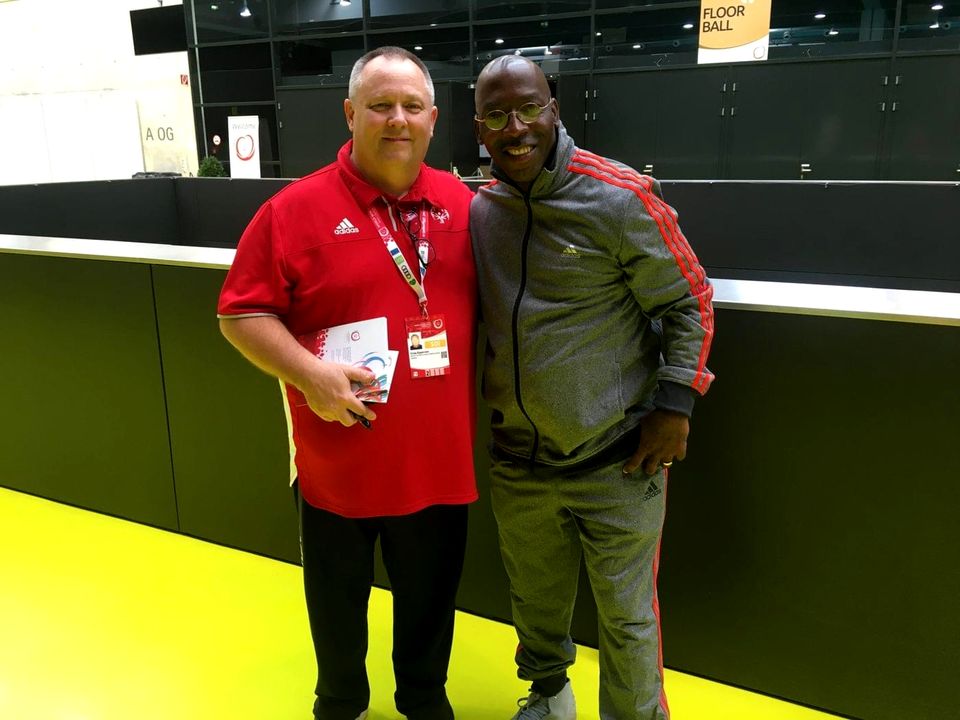 Doc Lewis with a man in a red Special Olympics jacket on a bright yellow court in Austria