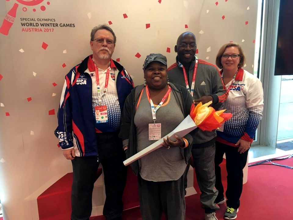 Doc Lewis with three Special Olympics volunteers, one holding a replica torch, at the World Winter Games in Austria, 2017