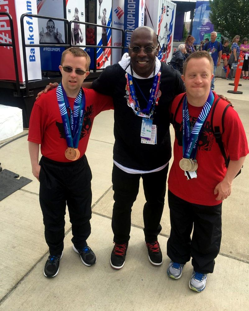 Doc Lewis with his arms around two Special Olympics athletes wearing their medals at the USA Games in Seattle, 2018